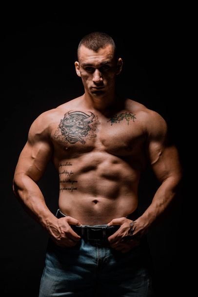 Portrait of young muscular man is flexing his muscles on dark background - Фото, изображение