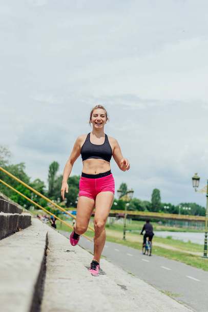 Fit healthy athlete, beautiful woman in tight sportswear jumping on stairs, warming up before jogging while looking highly motivated. - Фото, изображение