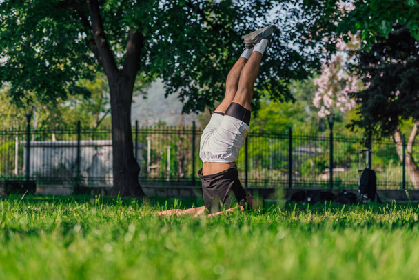 Young sporty handsome man practicing yoga in the park and doing the plow pose. - Photo, Image