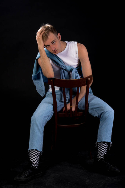 Portret modnego faceta w białej koszuli bez rękawów i niebieskich dżinsach siedzącego na chórze - Zdjęcie, obraz