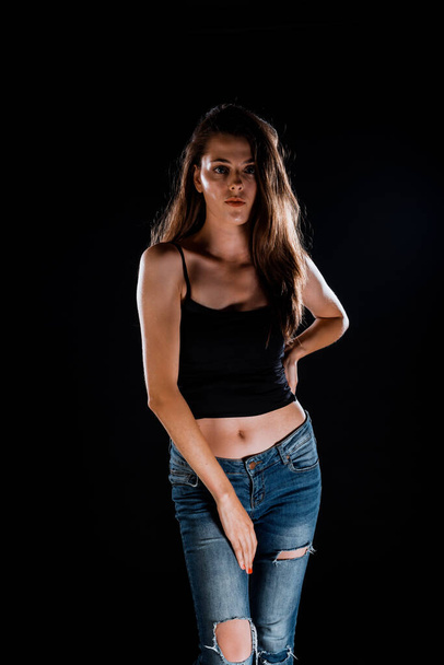 Portrait of a beautiful stylish girl wearing black tank top while posing over black wall - Photo, Image