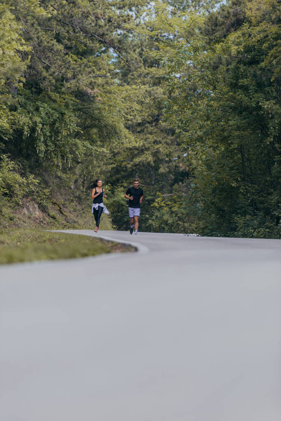 Athletic couple running on a street next to each other. Nature,fit and healthy concept. - Foto, immagini