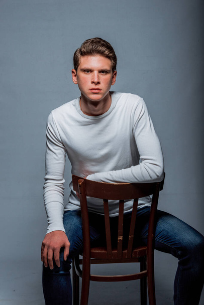 Studio fashion portrait of a young hipster man wearing black jumper and denim pants - Photo, Image