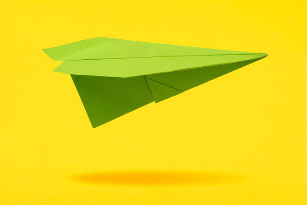 Green paper aircraft fly over yellow background - Foto, immagini