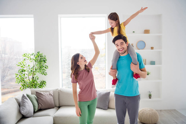 Photo of positive cheerful three people mom dad play weekend game carry shoulders small kid girl hold hand in house indoors - Foto, afbeelding