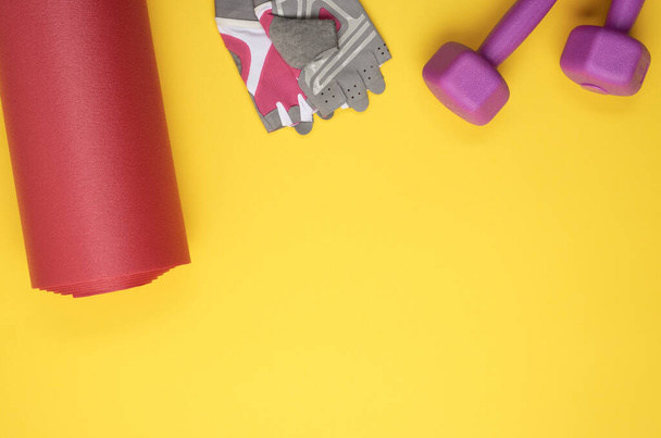 dumbbell e luvas de esportes, tapete de neoprene torcido para esporte de ioga no fundo amarelo, vista superior, espaço de cópia - Foto, Imagem