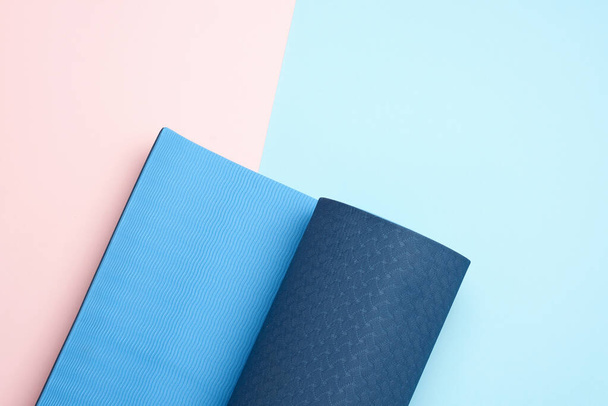 neopreen blauwe gedraaide mat ligt op een roze achtergrond, sportuitrusting, kopieerruimte - Foto, afbeelding