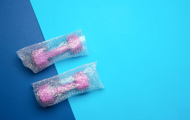 ein Paar lila Sporthanteln in einer transparenten Tasche auf blauem Hintergrund, Ansicht von oben, Kopierraum - Foto, Bild