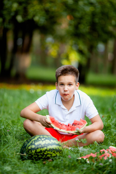 chico en camiseta blanca comiendo sandía en la hierba en el parque - Foto, imagen