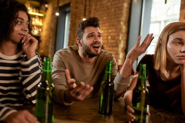 Friends looking disappointed while watching sports match on TV together, drinking beer and cheering for team in the bar. People, leisure, friendship and entertainment concept - Фото, зображення