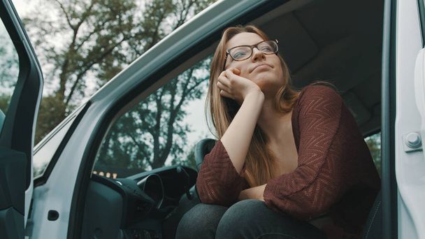 Νεαρή καυκάσια οδηγός γυναίκα με ανοιχτή πόρτα αυτοκίνητα κοιτάζοντας την απόσταση - Φωτογραφία, εικόνα