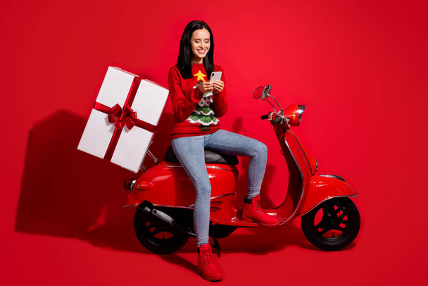 Portrait of her she nice attractive lovely cheerful girl sitting bike using device app delivering giftbox order shadow isolated over bright vivid shine vibrant red color background - Φωτογραφία, εικόνα