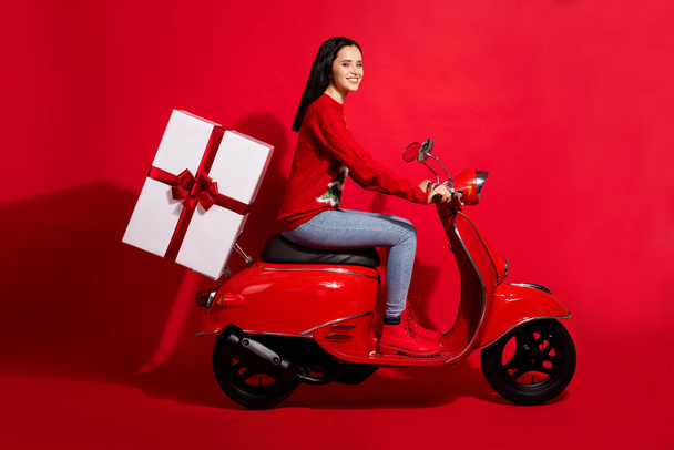 Profile side view portrait of her she nice attractive cheerful girl riding bike delivering bringing giftbox st Nicholas day isolated bright vivid shine vibrant red color background - Foto, immagini