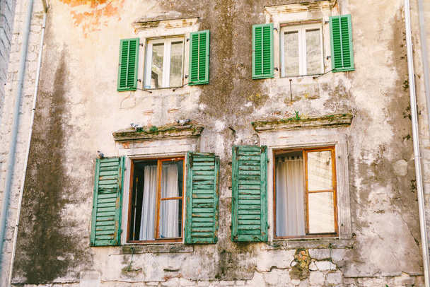An old multi-storey building with windows and wooden shutters with peeled paint. - Foto, Imagen