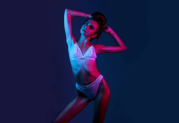 Skinny fashion model wear beige erotic lingerie in colorful bright neon uv red and blue lights, posing in studio hold long hair copy space - Fotografie, Obrázek