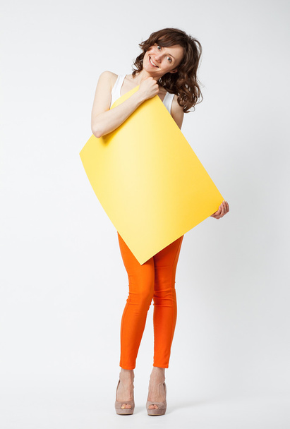 Playful young woman in orange pants holding yellow paper - Fotoğraf, Görsel