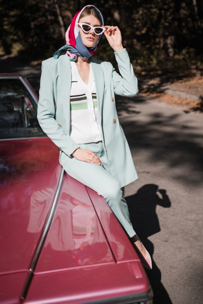 Young woman in sunglasses sitting on vintage car with road at background  - Фото, изображение