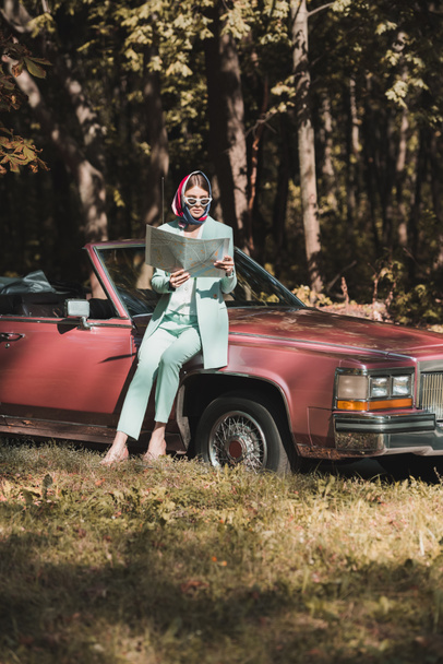 Elegante vrouw op zoek naar kaart in de buurt van auto tijdens de reis  - Foto, afbeelding