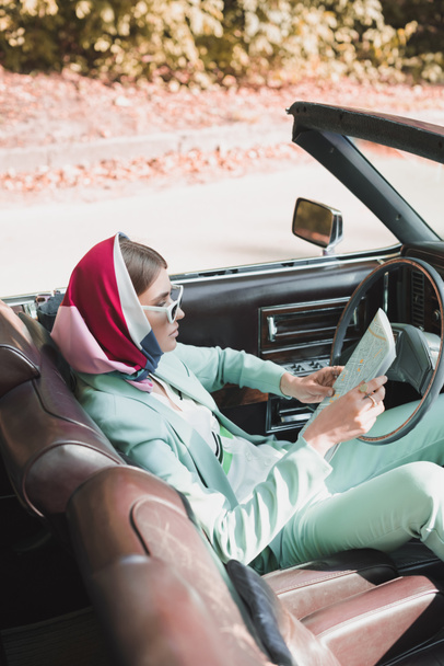 Femme élégante tenant carte tout en étant assis en voiture vintage sur le premier plan flou - Photo, image