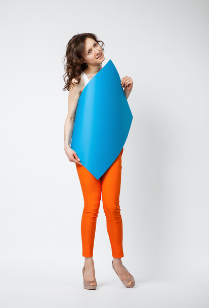 Beautiful young woman in orange pants holding blue paper - Foto, imagen
