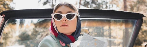 Elegancka kobieta w okularach przeciwsłonecznych i szaliku trzymająca mapę w samochodzie bez dachu, baner - Zdjęcie, obraz