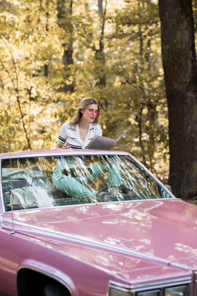 junge Frau sitzt im Cabrio und schaut im Wald auf Landkarte - Foto, Bild