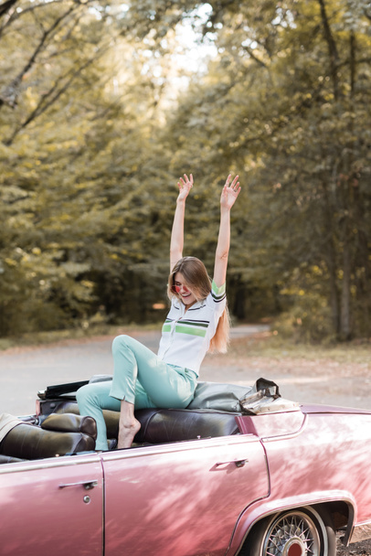 excited barefoot woman sitting in cabriolet with hands in air - Fotó, kép