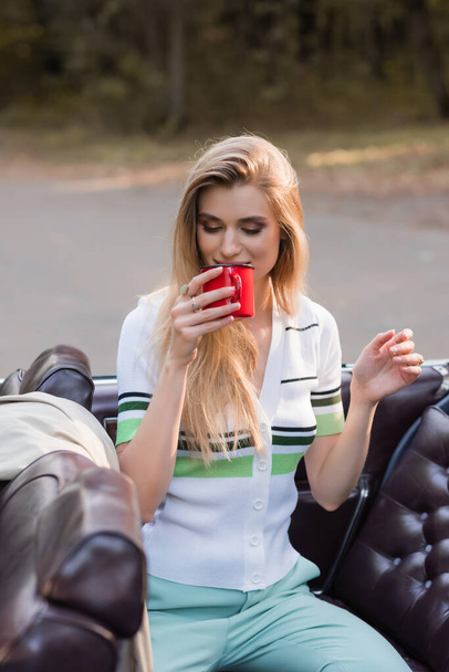 mujer elegante beber café mientras está sentado en cabriolet vintage en primer plano borrosa - Foto, Imagen