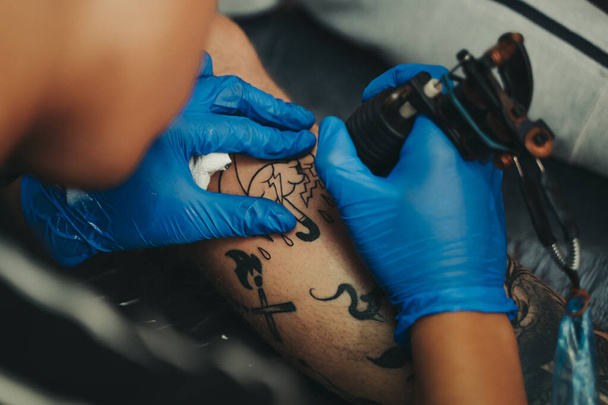 Joven tatuador tatuando la pierna de un cliente en su propio estudio. - Foto, Imagen