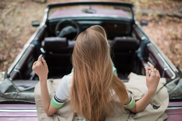 terug uitzicht op jonge vrouw zitten in vintage converteerbare auto op wazig achtergrond - Foto, afbeelding