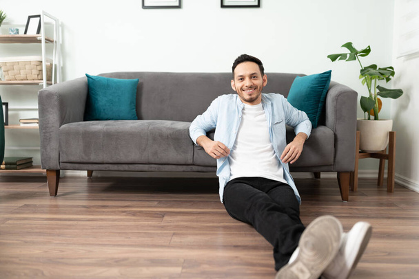 Good looking Latin man sitting on the floor and feeling comfortable in his new apartment - 写真・画像