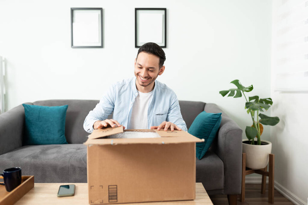 Attractive man looking happy while opening a package with some of the stuff he bought online - Foto, Bild