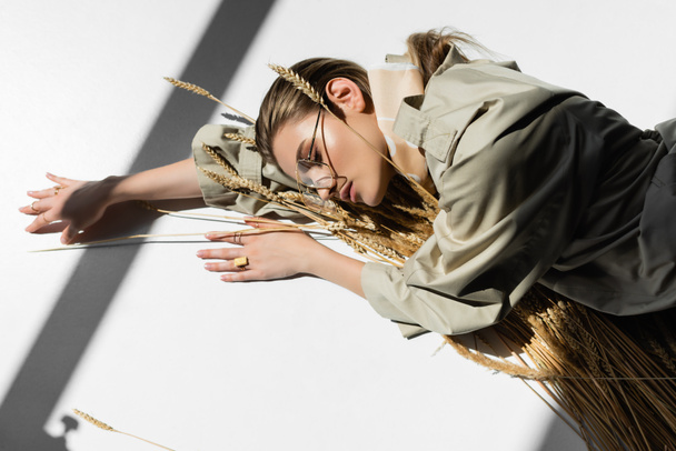young trendy woman in glasses lying with bunch of wheat spikelets on white - Photo, Image