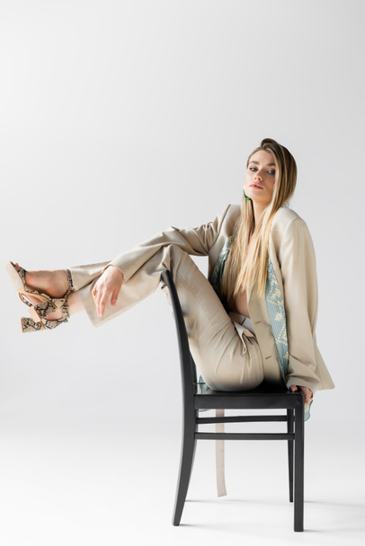 young stylish woman in suit sitting on wooden chair on white - Foto, afbeelding