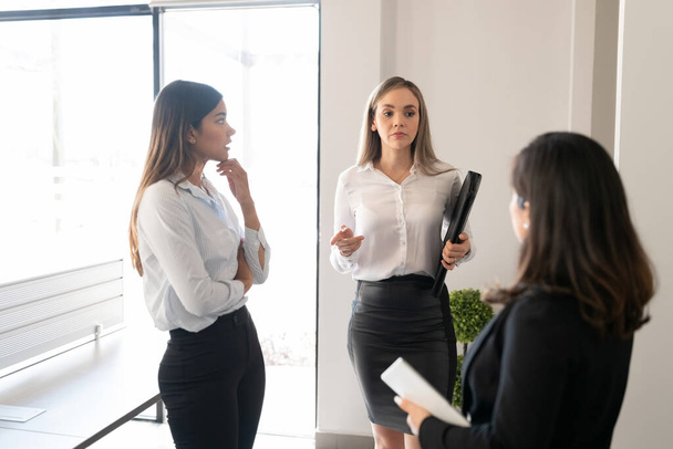 Female colleagues talking while having standing meeting in office - Photo, Image