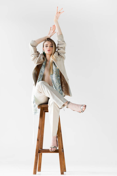 donna alla moda in abito seduta su sgabello in legno con mani sopra la testa su bianco - Foto, immagini