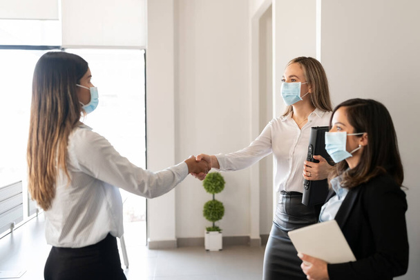 Empresarios con mascarillas protectoras estrechando la mano en la oficina durante la pandemia - Foto, Imagen