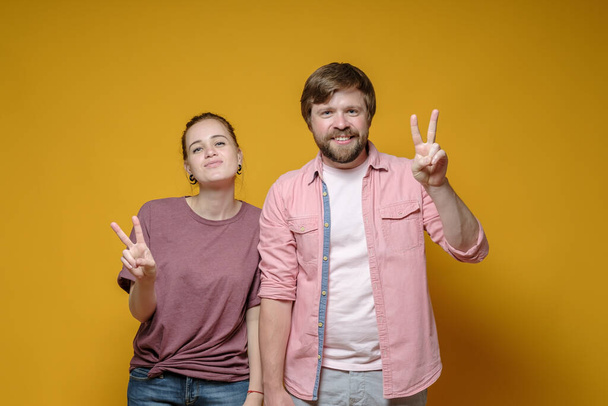 Contented, smiling man and woman in casual clothes make the V- sign with their fingers, a symbol of victory and peace.  - Фото, зображення
