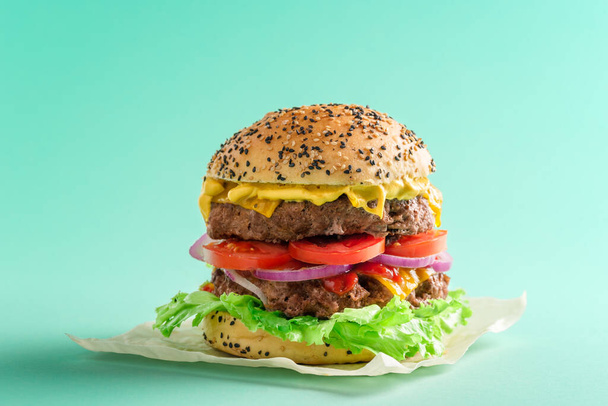 Házi hamburger egy zöld színű asztalon. Burger egy darab méhviasz ruhán. Nagy sajtburger minimalista zöld háttérrel. - Fotó, kép