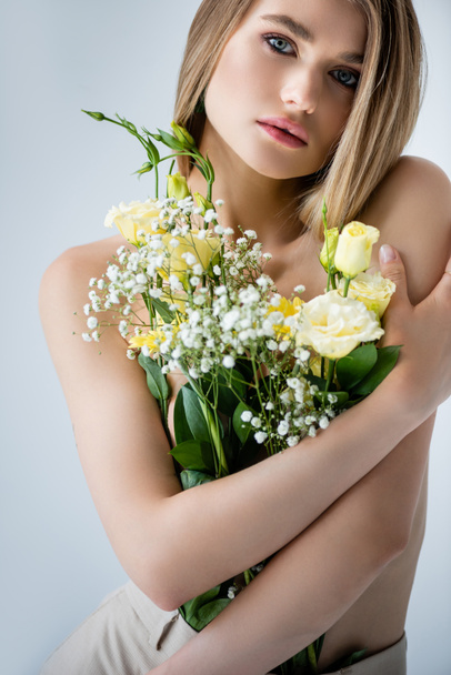 modelo jovem com ombros nus abraçando flores em cinza - Foto, Imagem