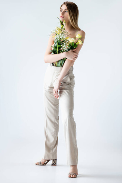 full length of young model with flowers in pants posing on white - Valokuva, kuva