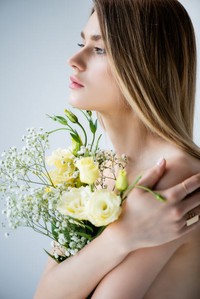 woman with naked shoulders embracing flowers on grey - Foto, imagen