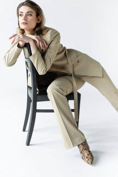 stylish woman in beige suit posing on wooden chair on white - Photo, Image