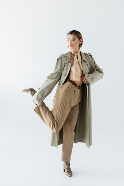 full length of trendy woman in glasses, trench coat and scarf posing on white - Photo, Image