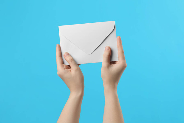 Woman holding white paper envelope on light blue background, closeup - Foto, Imagem