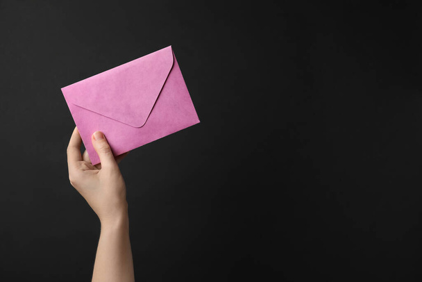 Woman holding pink paper envelope on black background, closeup. Space for text - Zdjęcie, obraz