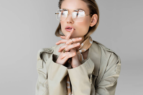 donna di tendenza in occhiali, trench e sciarpa in posa sul grigio - Foto, immagini