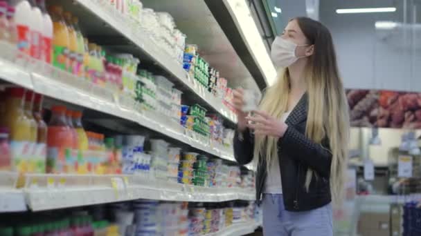 woman is choosing yogurt in supermarket, face mask for save - Filmati, video