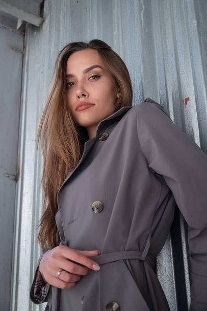 attractive young asian model in gray trench coat standing near wall outdoors - Fotografie, Obrázek