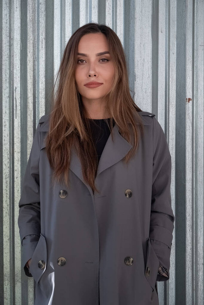 attractive young asian model in gray trench coat standing near metal fence - Φωτογραφία, εικόνα